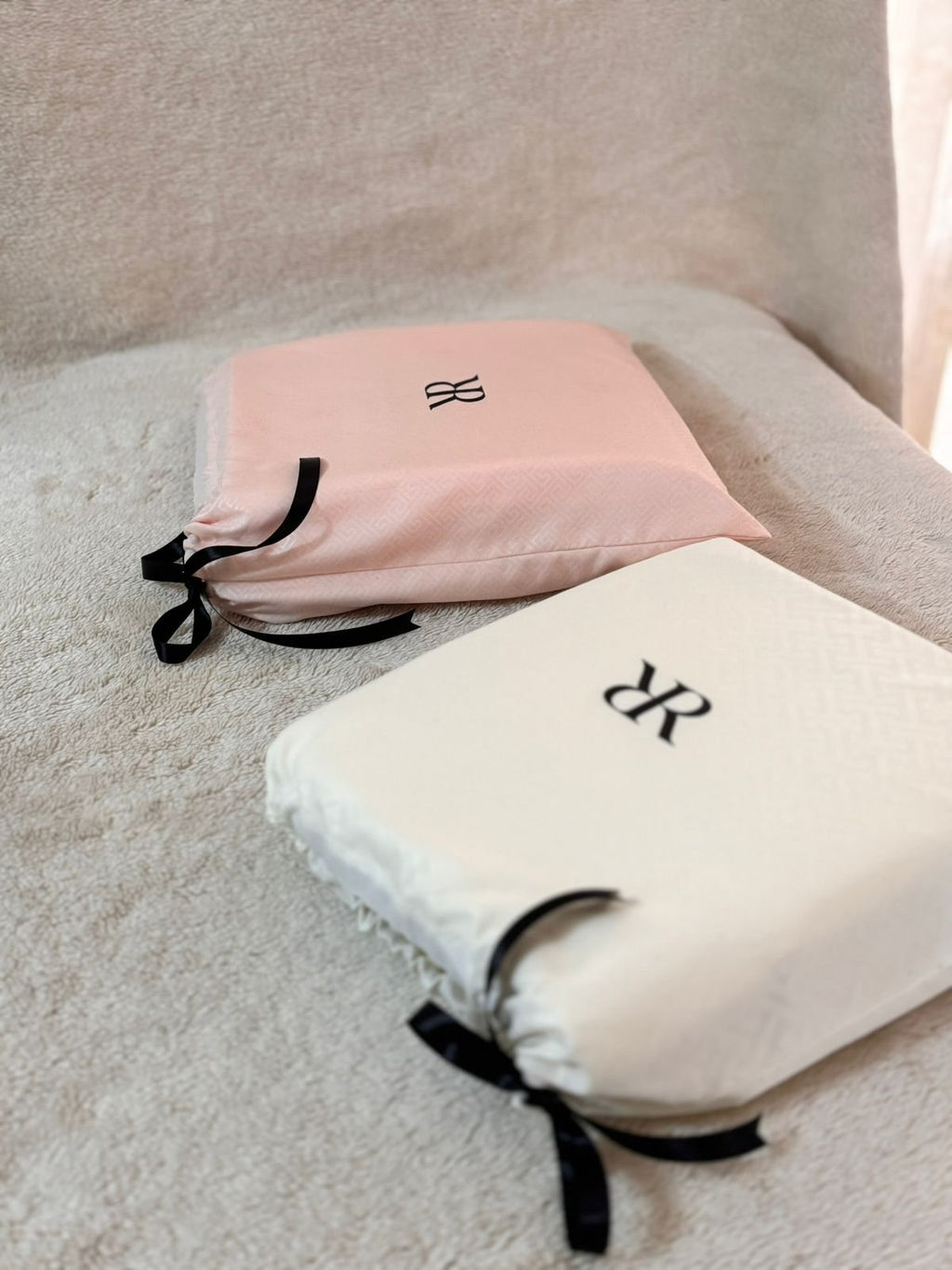 Dos juegos de sábanas Rosas Home apilados en sus bolsas de jacquard rosa y marfil