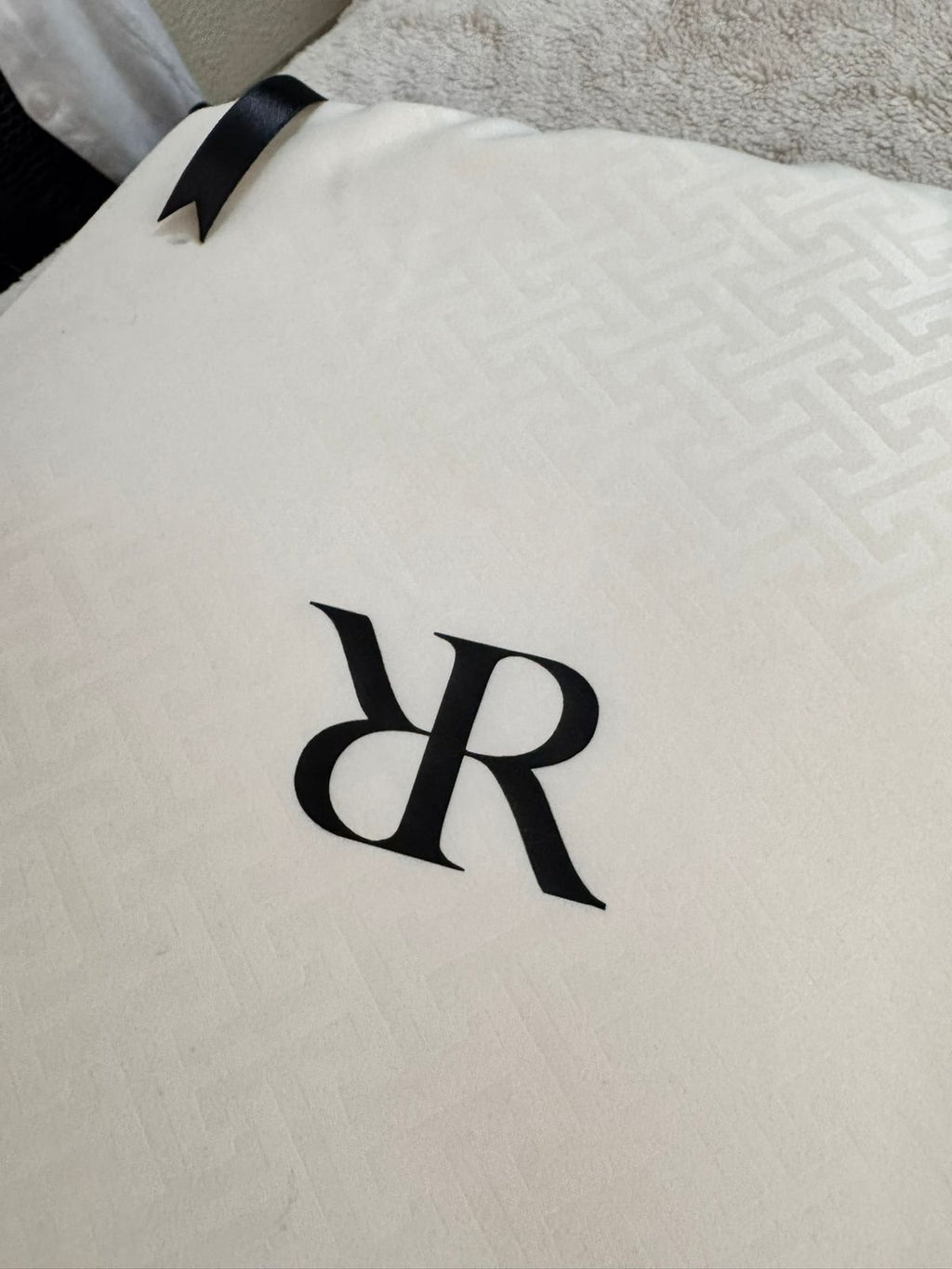 Primer plano del monograma RR sobre la bolsa de jacquard marfil de Rosas Home